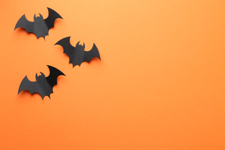 Halloween decor. Black paper bats on orange background, flat lay. Space for textの写真素材