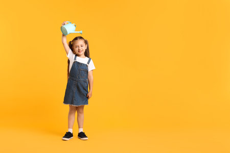 Little girl with watering can on orange background, space for text.の写真素材