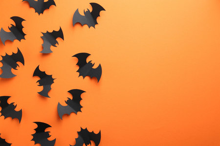 Halloween decor. Black paper bats on orange background, flat lay. Space for text