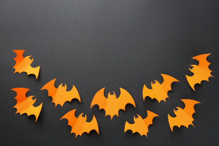 Halloween decor. Orange paper bats on black background, flat lay. Space for textの写真素材