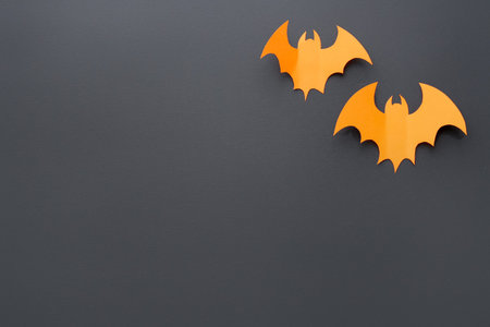 Halloween decor. Orange paper bats on black background, flat lay. Space for text