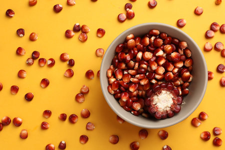 Piece of ripe red corn cob, bowl and kernels on yellow background, flat lay