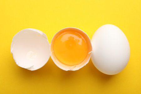 Whole and broken chicken eggs on yellow background, flat layの写真素材
