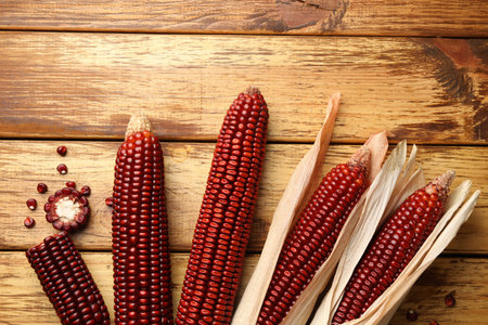Ripe red corn cobs on wooden table, flat lay