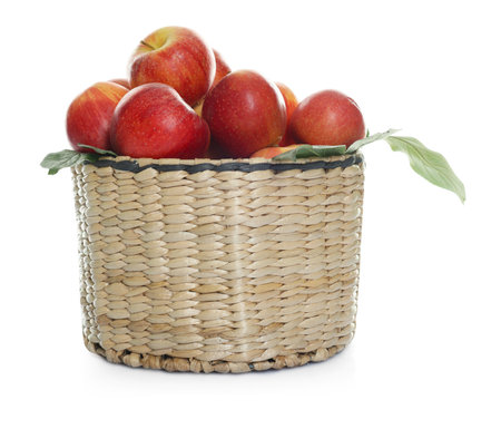 Fresh apples in wicker basket and green leaves isolated on whiteの写真素材