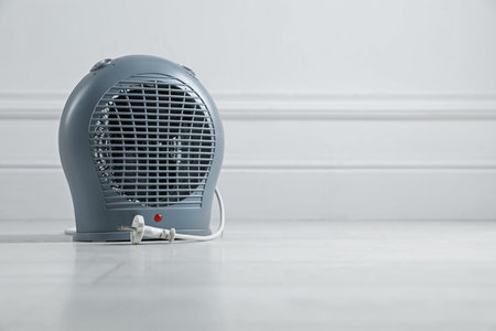 Electric fan heater on floor near light gray wall indoors, closeup. Space for textの写真素材