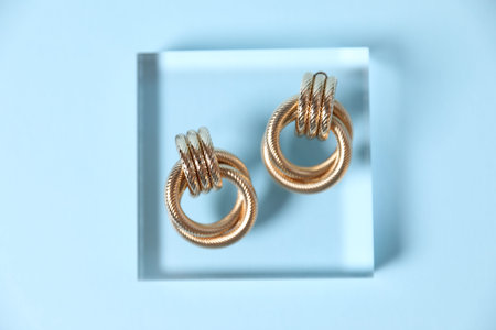 Beautiful gold earrings on light blue background, top view