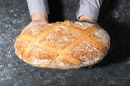 Baker with loaf of fresh bread at gray textured table, top view