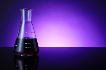 Flask with color liquid on table against violet background. Space for textの写真素材