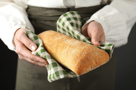 Woman holding freshly baked bread on black background, closeup