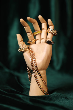 Mannequin hand with beautiful gold jewelry against dark green clothの写真素材