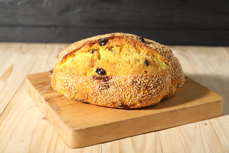 Loaf of fresh bread with raisins on light wooden table, closeup