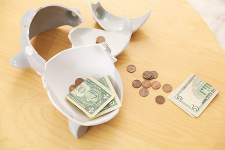 Pocket money. Broken piggy bank with dollars and coins on wooden table indoors, above viewの写真素材