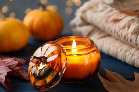 Autumn composition with burning candle on blue wooden table against blurred lights, closeupの写真素材