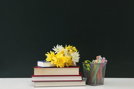 Happy teacher's day. Flowers, books and stationery on white table against chalkboard. Space for text