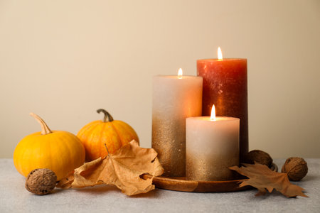 Autumn composition with burning candles and pumpkins on gray table against beige backgroundの写真素材