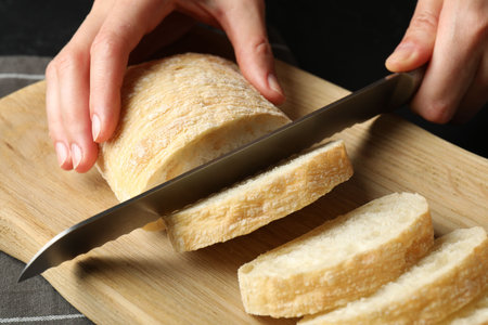 Woman cutting fresh crispy ciabatta at black table, closeup