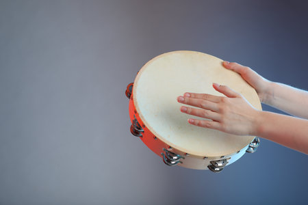 Woman playing tambourine on gray background, closeup. Space for textの写真素材