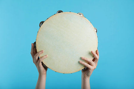 Woman playing tambourine on light blue background, closeup