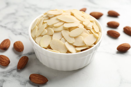 Fresh almond flakes and whole nuts on white marble table, closeupの写真素材
