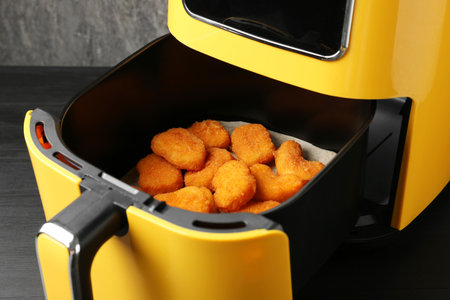 Air fryer container with cooked chicken nuggets on black table, closeupの写真素材