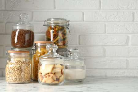 Glass jars with different products on white marble table. Space for textの写真素材