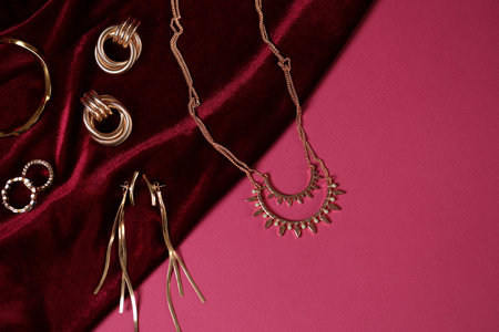 Stylish presentation of gold jewelry and red cloth on pink background, flat lay. Space for textの写真素材