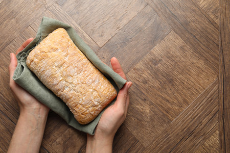 Woman holding fresh bread at wooden table, closeup. Space for textの写真素材
