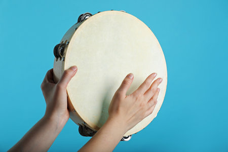 Woman playing tambourine on light blue background, closeupの写真素材