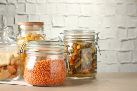 Glass jars with different products on wooden table, closeup. Space for textの写真素材