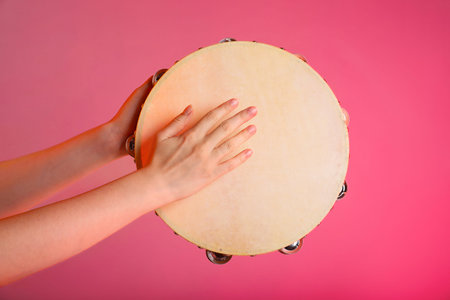 Woman playing tambourine on pink background, closeup