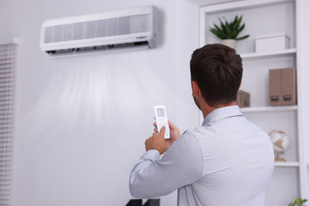 Man switching on air conditioner with remote control in officeの写真素材