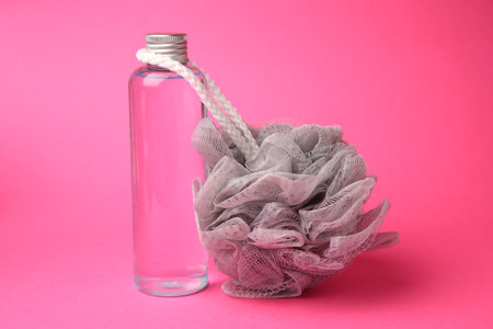 Gray shower puff and bottle of cosmetic product on pink backgroundの写真素材