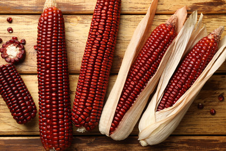 Ripe red corn cobs on wooden table, flat lay
