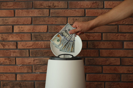 Man throwing dollar banknotes into trash bin near brick wall, closeupの写真素材