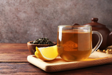 Aromatic tea in cup with lemon, teapot and dry leaves on wooden table, closeup. Space for textの写真素材