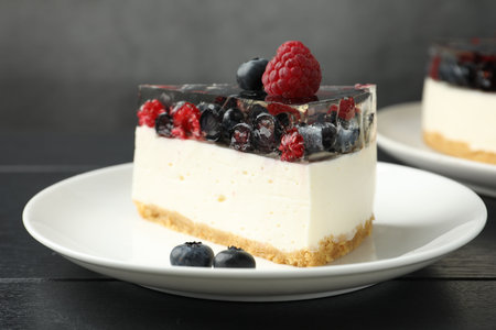 Piece of cheesecake with berries on black wooden table, closeup