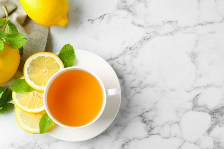 Aromatic tea in cup with lemons and mint on white marble table, flat lay. Space for textの写真素材