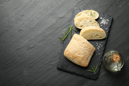 Cut crispy ciabatta, rosemary, salt and oil on black textured table, flat lay. Space for textの写真素材