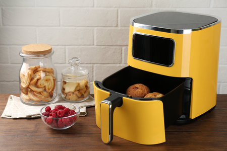 Freshly baked muffins in air fryer, raspberries and cookies on wooden table against white brick wallの写真素材