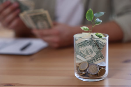 Glass jar with money and seedling. Man budgeting at desk, selective focus