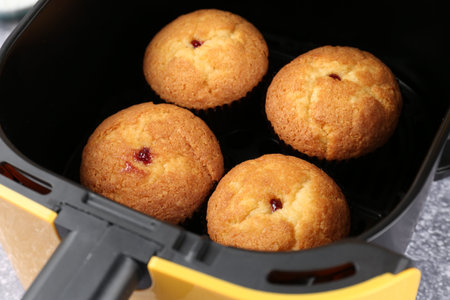 Freshly baked muffins in air fryer on gray textured table, closeup