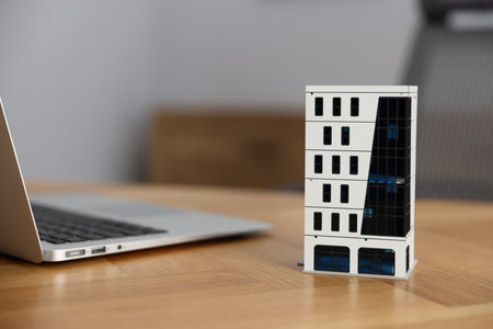 Real estate. Apartment building model and laptop on table indoors, closeup. Space for textの写真素材