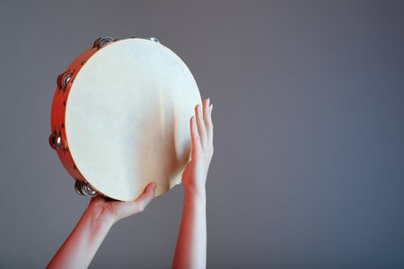 Woman playing tambourine on gray background, closeup. Space for textの写真素材