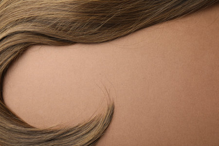 Lock of beautiful hair on light brown background, top view. Space for textの写真素材