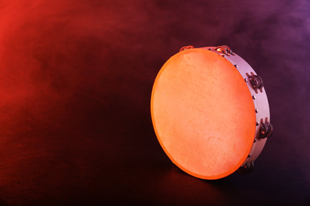 Tambourine in color light on dark background with smoke. Space for textの写真素材