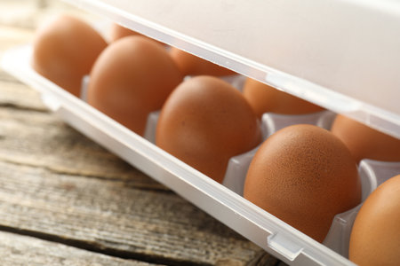 Raw chicken eggs in container on wooden table, closeupの写真素材