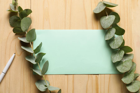 Blank card, pen and eucalyptus branches on wooden table, flat layの写真素材