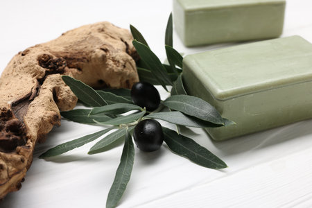 Handmade soap bars, olives, and green leaves on white wooden table, closeupの写真素材
