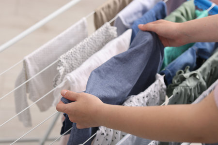 Woman putting clean baby clothes onto drying rack indoors, closeupの写真素材